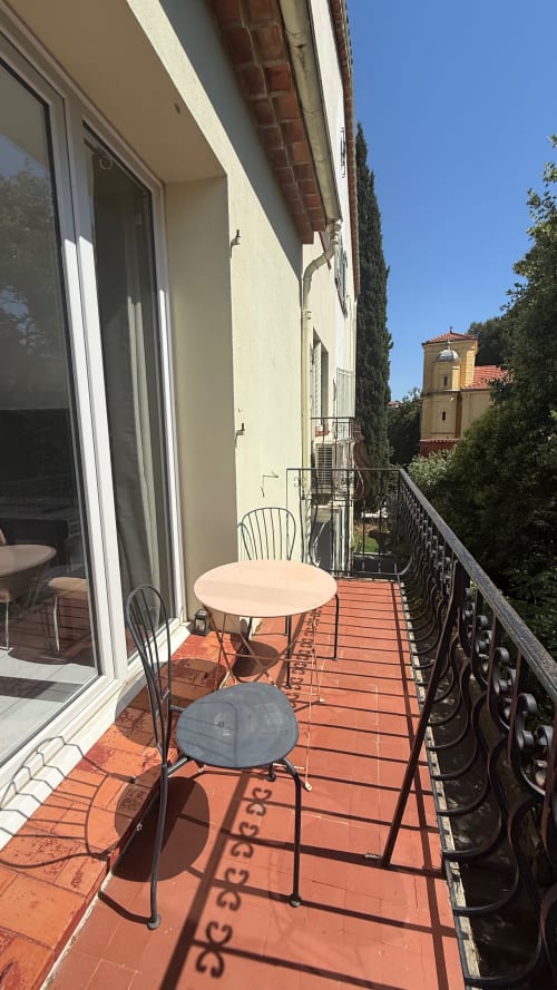 Terrasse ensoleillée de la Kimi Résidence à Cannes avec table ronde, chaises, carrelage en terre cuite et vue sur le jardin