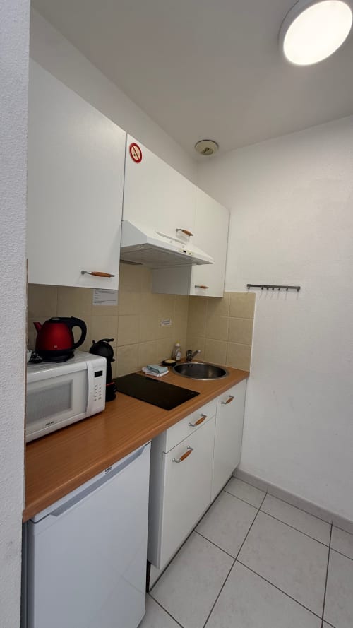 Petite kitchenette à la Kimi Résidence à Cannes avec meubles blancs, plan de travail en bois, micro-ondes, bouilloire électrique et carrelage