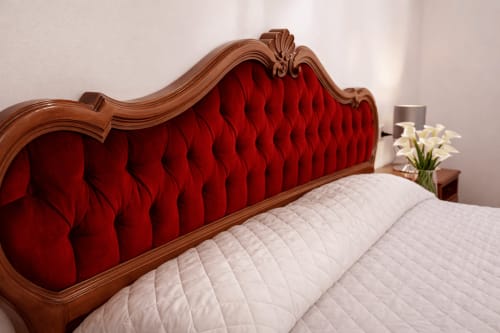 Testata del letto lussuosa in velluto rosso trapuntato con cornice in legno intagliato su biancheria bianca all'Hotel Ariel Silva Venezia