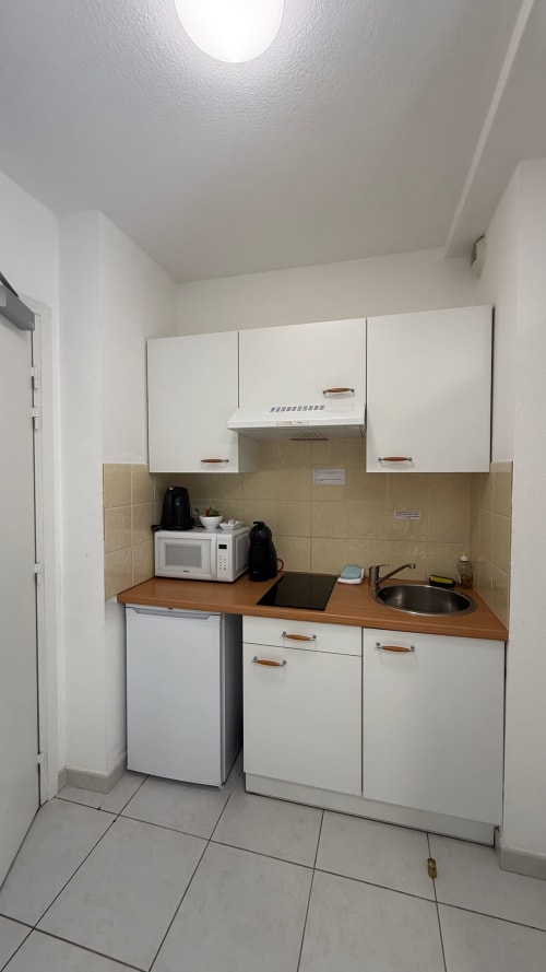 Kitchenette compacte du Twin Studio à Kimi Résidence Cannes avec placards blancs, plan de travail en bois et carrelage beige