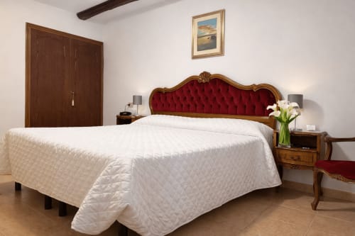 Elegante dormitorio con colcha acolchada blanca, cabecero de terciopelo rojo y muebles de madera en Hotel Ariel Silva Venecia