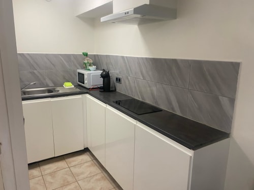 Kitchenette moderne à la Kimi Résidence Cannes : meubles blancs, plan de travail noir, crédence carrelage gris