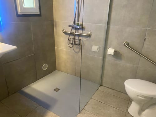 Salle de bain moderne à la Kimi Résidence à Cannes avec douche à l'italienne, porte en verre, toilettes blanches et murs en carrelage beige