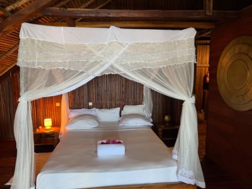 Lit à baldaquin élégant avec rideaux blancs vapoureux au Madabay's Lodge à Nosy Be, Madagascar