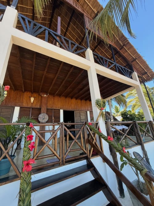 Villa en bord de mer au Madabay's Lodge Nosy Be avec terrasse en bois, toit de chaume, fleurs roses et vue sur mer