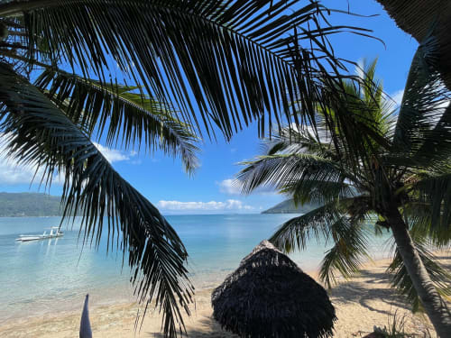 Vue de villa tropicale à Madabay's Lodge Nosy Be avec palmiers, sable blanc, eaux turquoise et îles lointaines