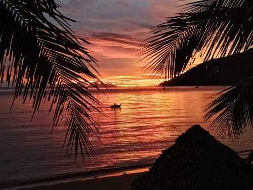 Coucher de soleil tropical à la villa du Lodge Madabay à Nosy Be, lumière dorée se reflétant sur la mer à travers les palmes