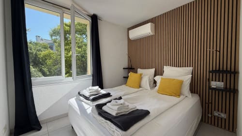 Chambre moderne à la Kimi Résidence à Cannes avec lit queen-size, touches jaunes, mur à lames de bois, climatisation et jardin