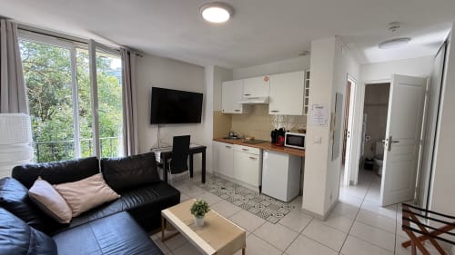 Appartement moderne à Kimi Résidence Cannes avec canapé noir, kitchenette, TV écran plat et vue sur le jardin depuis la terrasse