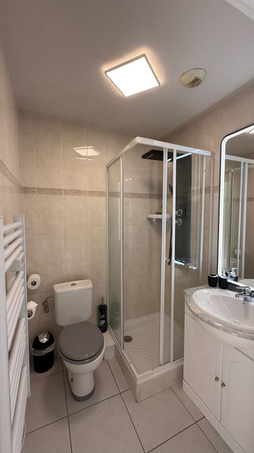 Salle de bain moderne à la Kimi Résidence à Cannes avec douche, toilettes, vasque blanche et éclairage LED au plafond