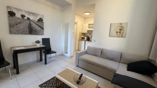 Spacieux séjour moderne à la Kimi Résidence de Cannes : canapé gris, bureau, kitchenette et œuvres d'art sur murs blancs