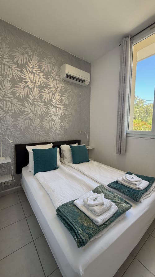 Chambre moderne à la Kimi Résidence à Cannes avec lits jumeaux, oreillers turquoise, vue sur le jardin et climatisation