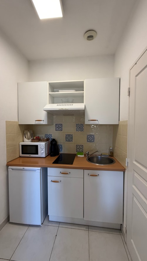 Petite kitchenette à la Résidence Kimi, Cannes, avec armoires blanches, plan de travail en bois, micro-ondes, évier et cuisinière