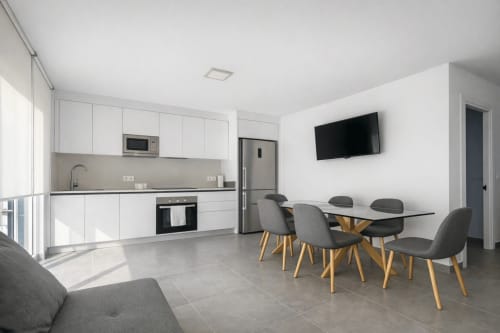 Cocina americana y comedor modernos en apartamento de Baiona con muebles blancos, mesa de comedor y TV de pared