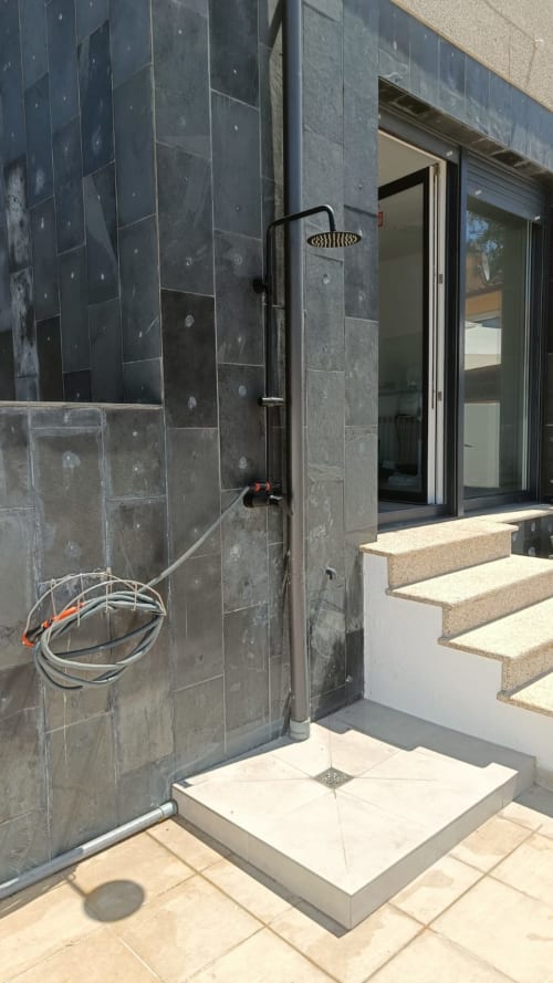 Moderna zona de ducha exterior en el apartamento Bahía Rental de Baiona con azulejos de pizarra oscura y alcachofa de lluvia