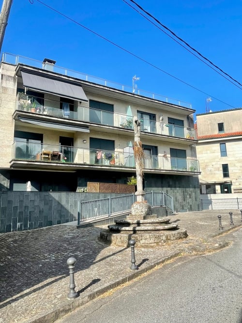 Edificio de apartamentos en Baiona con terrazas modernas, barandillas metálicas y fuente en patio central en día soleado