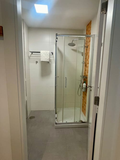 Baño moderno con ducha de cristal, azulejos blancos y alcachofa de lluvia en el apartamento Bahía Rental de Baiona