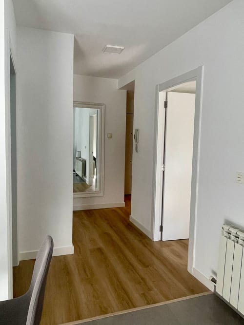 Moderno pasillo de apartamento en Bahía Rental, Baiona, con suelos de madera, paredes blancas y múltiples puertas