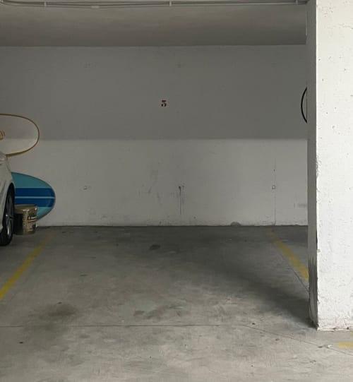 Espacio de aparcamiento vacío en el garaje subterráneo del complejo Baiona-Atlántico con paredes blancas y marcas amarillas en el suelo
