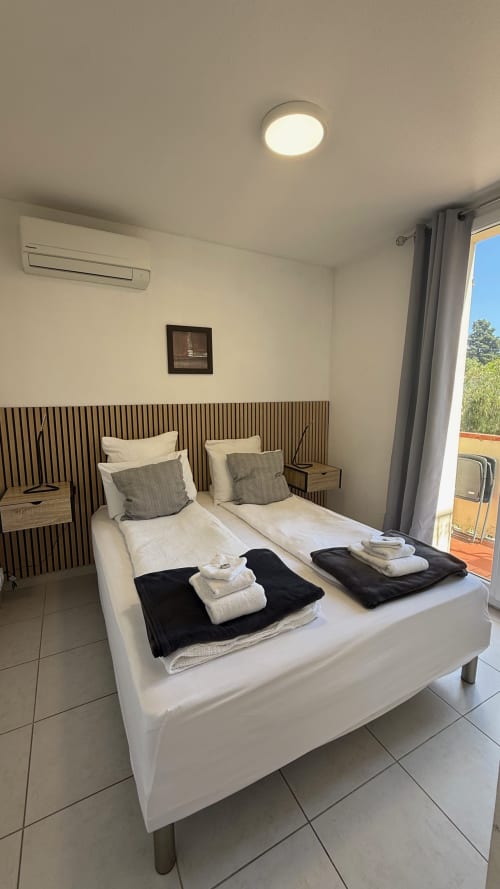 Lits jumeaux aux draps blancs et serviettes roulées dans une chambre lumineuse de la Kimi Résidence Cannes, avec accès à la vue sur le jardin