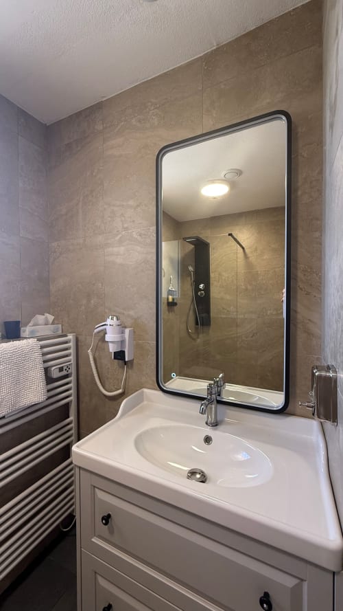 Vasque blanche élégante, miroir à cadre noir et murs carrelés beige - Kimi Résidence, Cannes