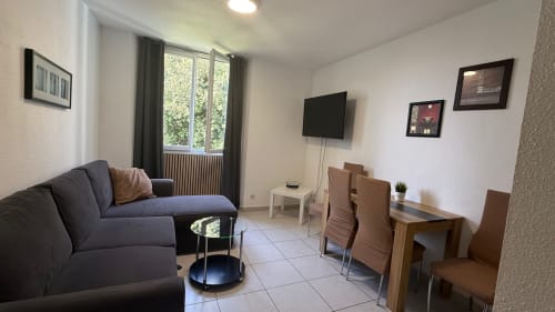 Séjour de la Suite Familiale à Kimi Résidence, Cannes avec canapé, table à manger, TV et vue sur le jardin par les portes-fenêtres