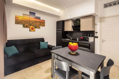 Modern Taormina apartment living area with black kitchen, dining table, black sofa, and sunflower artwork on cream walls.