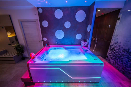 Neon-lit spa bathroom in Taormina apartment with illuminated hot tub, purple ambient lighting, and circular wall art