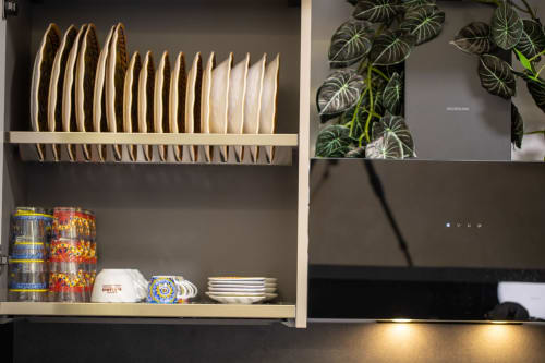 Modern kitchen shelving with stacked dinnerware, decorative bowls, canned goods, and trailing potted plant in Taormina