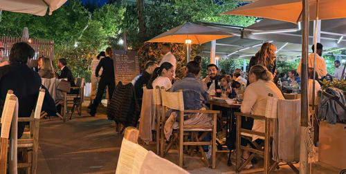 Evening outdoor dining at Cannes hotel with wooden tables, orange umbrellas, and lush greenery ambiance.