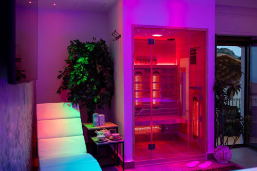 Modern spa sauna with red and magenta neon lighting, green plant, and ambient colored seating at Suite Apartment Taormina