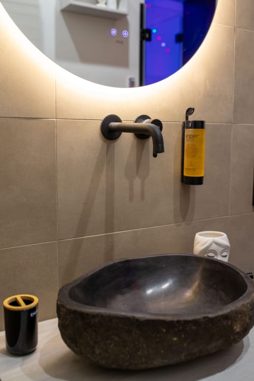Modern bathroom at Suite Apartment Taormina with black stone bowl sink, wall-mounted faucet, illuminated round mirror, and