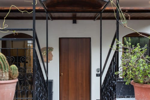 Mediterranean-style apartment entrance in Taormina with dark wooden door, black wrought iron railings, potted plants, and