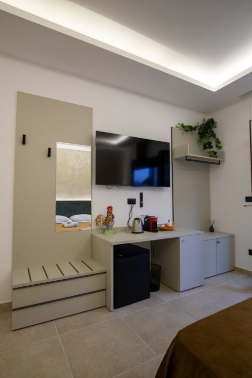 Modern suite at Taormina hotel with bed, wall-mounted TV, kitchenette, and contemporary furnishings under skylight
