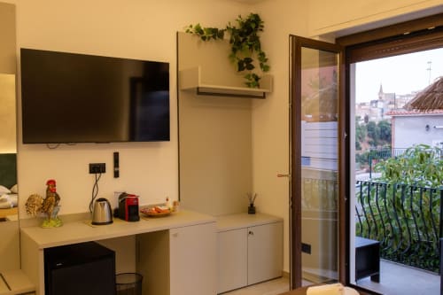 Modern hotel room in Taormina with wall-mounted TV, kitchenette, and glass balcony door overlooking city views