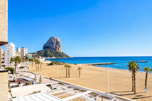 Playa de Calpe con la formación rocosa de Peñyal d'Ifach, arena blanca, palmeras y modernos apartamentos en Riurau Home