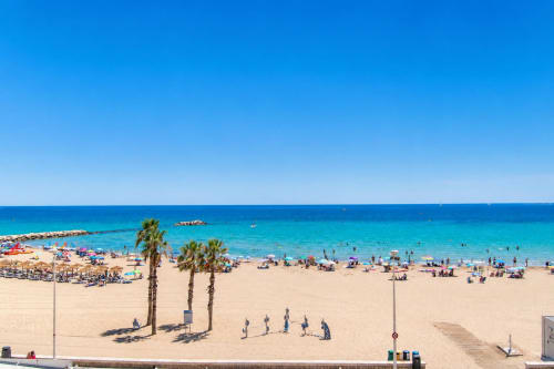 Playa de Calpe con arena dorada, palmeras y mar Mediterráneo turqueso en el apartamento Riurau Home