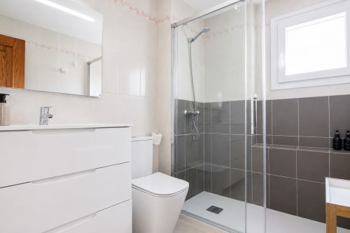Baño moderno con ducha accesible, tocador blanco y detalles en azulejos grises en Riurau Home, Calpe