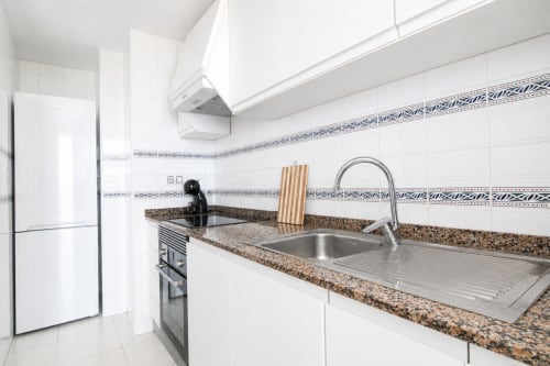 Cocina moderna con encimera de granito, fregadero de acero inoxidable, armarios blancos y backsplash de azulejos decorativos en Riurau Home