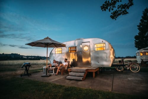 Remolque Airstream vintage en B&B Wine And Cooking Penedès de Barcelona, con huéspedes cenando bajo sombrilla al atardecer