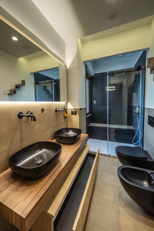 Modern bathroom in Taormina suite with dual black vessel sinks, wooden vanity, walk-in shower with glass enclosure, and