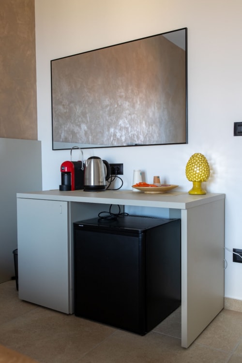 Modern hotel room desk with flat-screen TV, red coffee machine, kettle, and yellow lamp in Suite Apartment Taormina