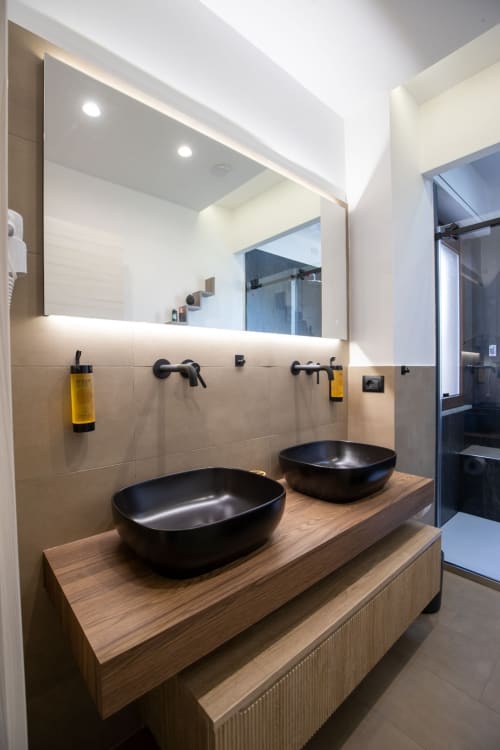 Modern bathroom with dual black vessel sinks on wooden vanity, illuminated mirror, and black fixtures at Suite Apartment