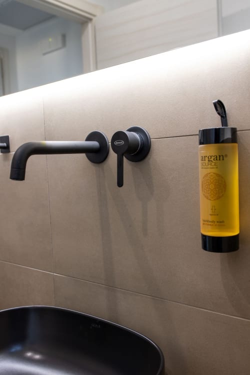 Modern black wall-mounted faucet and argan body wash in bathroom of Suite Apartment Taormina's superior sea view room