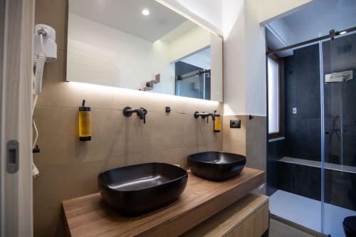 Modern bathroom in Taormina suite with dual black vessel sinks on wooden counter, large mirror, walk-in shower with glass