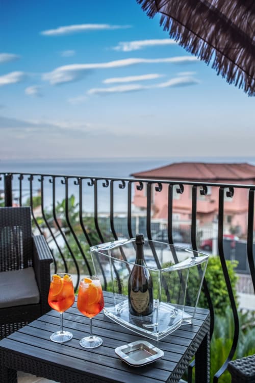 Balcony overlooking Taormina's Ionian Sea with Aperol Spritz cocktails and champagne bottle, red umbrellas, and coastal