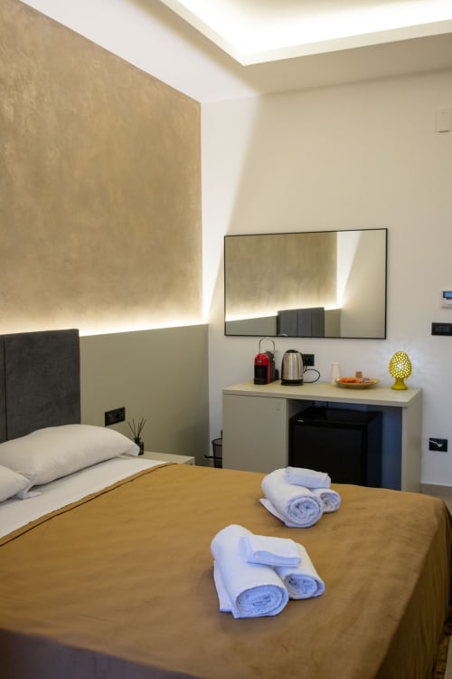 Modern hotel bedroom at Suite Apartment Taormina with sea view, featuring gold-lit accent wall, vanity desk, and rolled