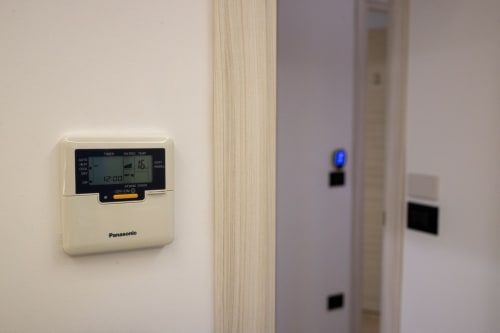 Panasonic programmable thermostat displaying 12:00 on wall in Taormina suite apartment with air conditioning control