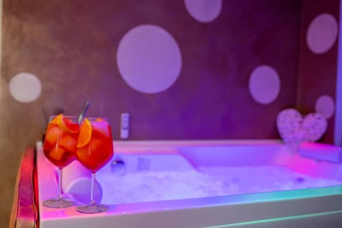 Two red cocktails with orange slices on a modern balcony overlooking Taormina, with purple ambient lighting and bokeh lights