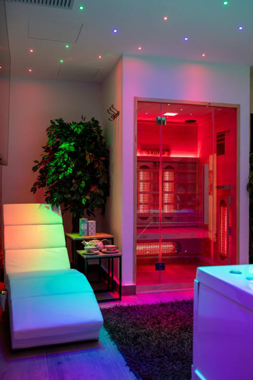 Modern spa suite with red infrared sauna, neon lighting, glowing lounge furniture, and tropical plants at Suite Apartment